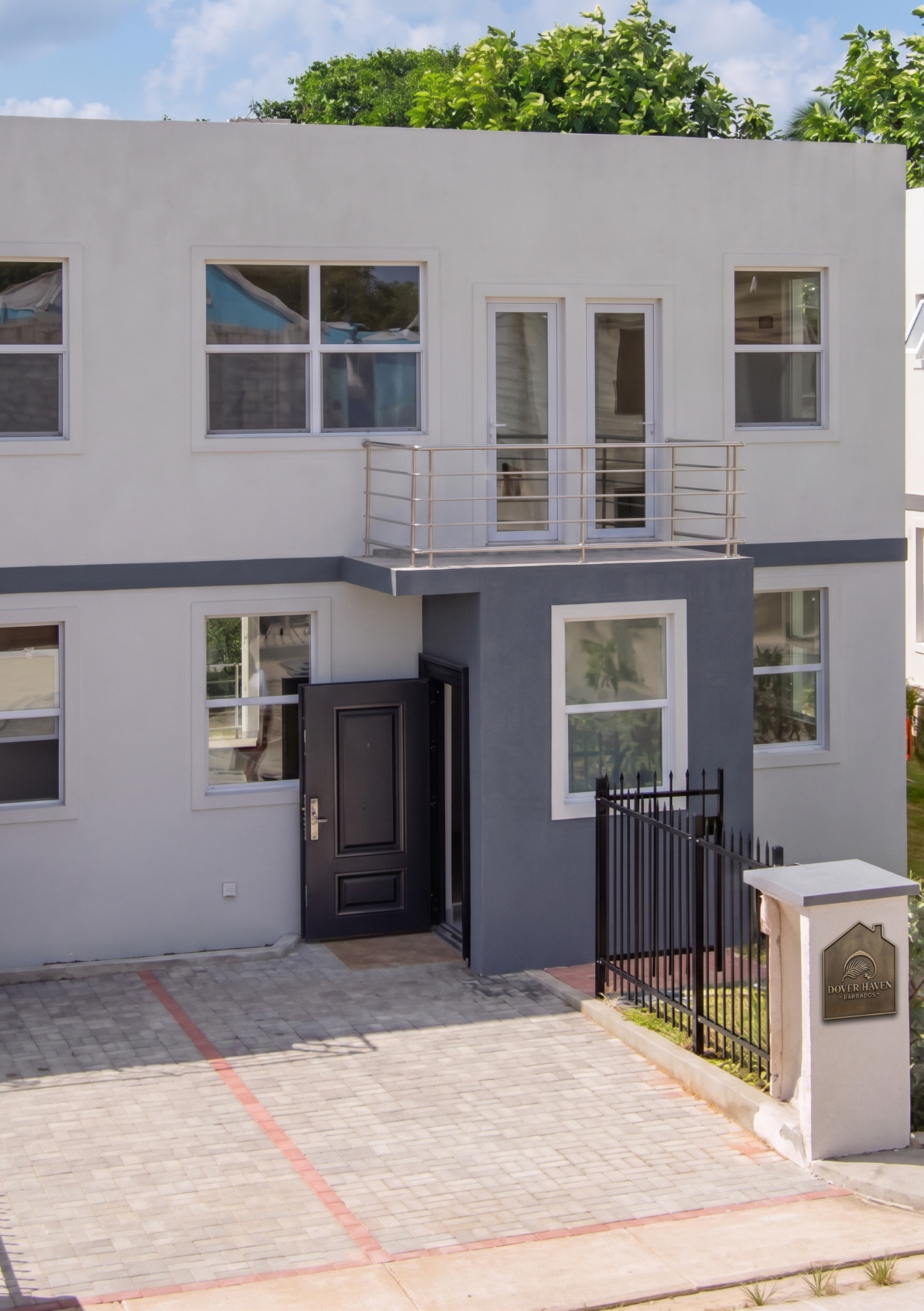 The front of Dover Haven at Dover Mews: a two-storey cream and grey townhouse with a first-floor balcony, dark front door and paved driveway.